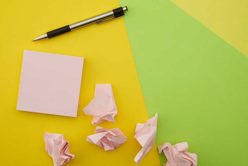 A post-it note stack on a desk with a pen and a few wrinkled notes scattered around.